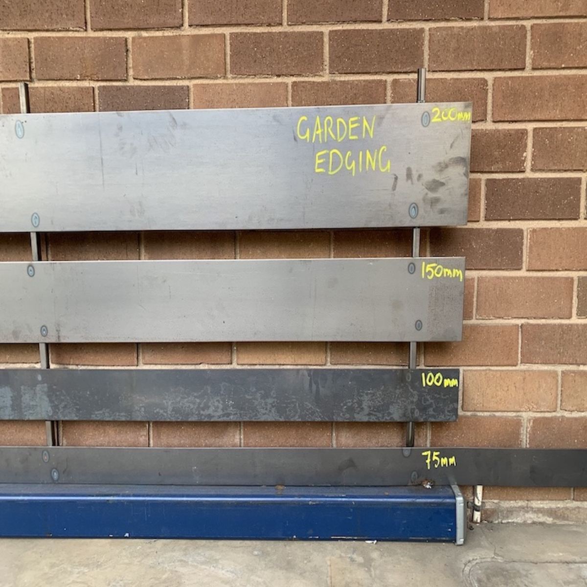 Steel garden edging in four depths displayed against a brick wall